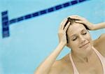 Woman smiling with hands on head, pool in background