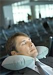 Man resting with neck pillow in airport lounge