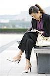 Young businesswoman sitting on bench looking down at cell phone