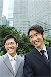 Two young businessmen, laughing, office building in background