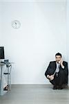 Businessman sitting on floor, in corner, talking on phone