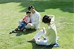 Family sitting on grass, woman taking photo of man and boy