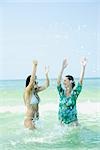 Two young women standing waist deep in sea, splashing