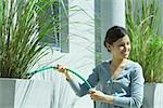 Young woman watering outdoor plants with hose