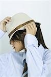 Teenage girl wearing shirt and tie, pulling hat down over eyes, portrait