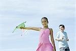 Girl holding out kite, boy in background