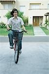 Teen boy riding bicycle in residential neighborhood, full length
