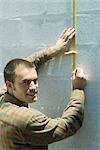Man measuring wall with measuring tape, smiling over shoulder at camera