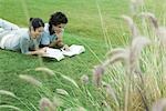 Young adult couple reading outdoors, lying on grass