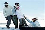 Girl sitting on ground, on snowboard, being pulled up by friends