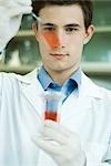 Young male lab worker holding up microscope slide and beaker