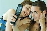 Two young friends photographing selves with cell phone, smiling