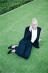 Businesswoman sitting on grass, using cell phone, high angle view
