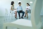 Three business associates sitting in chairs, discussing, full length