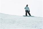 Young man snowboarding on top of ski slope, full length