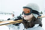 Two young skiers carrying ski on shoulder, looking away, close-up