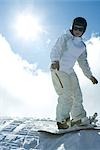 Young snowboarder standing on top of hill, looking at camera, full length portrait