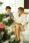 Couple sitting on couch, making a toast with champagne, smiling