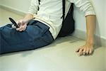 Male student sitting on the floor, holding cell phone, cropped view