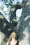 Blonde woman leaning against tree, eyes closed, low angle view