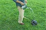 Man standing on grass, watering pile of stones with watering can, waist down