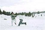 Two young male friends roughhousing in snow, full length