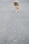 Boy placing trail of pebbles on asphalt