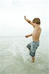 Boy splashing ankle-deep in water, side view