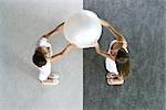 Teen twin sisters holding up ball together, viewed from directly above