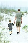 Teenage boy and little brother walking at the beach, holding hands, rear view