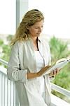 Woman standing on porch reading book