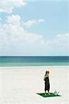 Girl standing on square of artificial turf on beach, next to watering can, high angle view