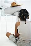 Girl sitting on floor, listening to mother reading book, rear view, cropped