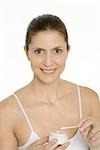 Woman holding cotton swab and jar of moisturizer, smiling at camera