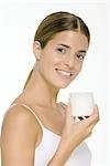 Woman holding up jar of skin cream, smiling at camera