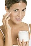 Woman applying moisturizer to face, smiling at camera