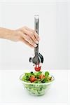 Woman picking tomato out of salad bowl using tongs, cropped view of hand