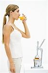 Young woman standing in front of citrus press, drinking freshly squeezed orange juice