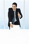 Businessman leaning on back of chair, giving thumbs up to camera