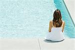 Woman sitting on edge of swimming pool, rear view, high angle