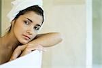 Woman resting head against side of bathtub, looking away, close-up