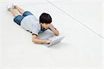 Boy lying on stomach on the ground, using laptop computer