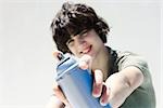 Teenage boy pointing can of spray paint at camera, focus on the foreground