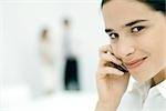 Woman using cell phone, smiling at camera, close-up