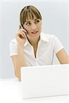 Woman sitting in front of laptop computer, using cell phone, looking away