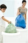 Young woman and boy placing garbage bags in separate garbage cans