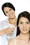 Hair stylist spraying woman's hair, both smiling at camera