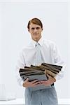 Professional man carrying a disorganized stack of binders, looking at camera