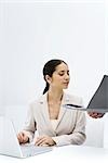Woman looking at a folder being held open for her, using laptop computer