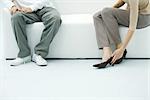 Man and woman sitting on sofa, woman putting on shoe, cropped view